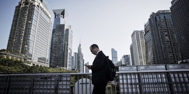 A pedestrian using a smartphone walks along a pedestrian bridge as commercial buildings stand in the background in Shenzhen, China, on Wednesday, Dec. 16, 2015. China's leaders signaled they will take further steps to support growth, including widening the fiscal deficit and stimulating the housing market, to put a floor under the economy's slowdown. Photographer: Qilai Shen/Bloomberg via Getty Images