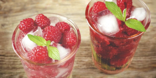 Summer juice with fresh raspberries mint and ice in a glass on a dark wood