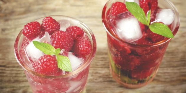 Summer juice with fresh raspberries mint and ice in a glass on a dark wood background.