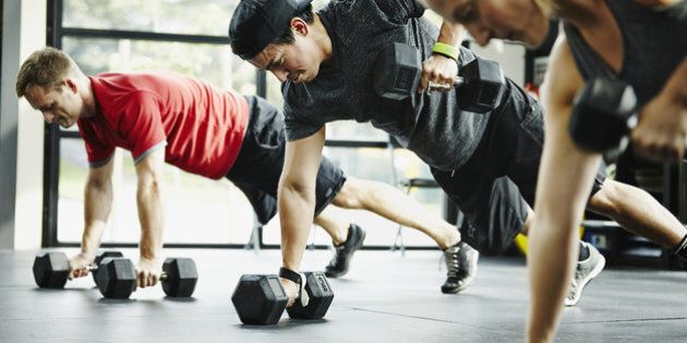 Group of friends doing pushups with dumbbells in crossfit gym