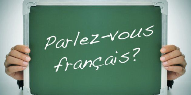 man wearing a suit holding a chalkboard with the question parlez-vous francais? do you speak french? written in it