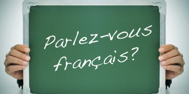 man wearing a suit holding a chalkboard with the question parlez-vous francais? do you speak french? written in it