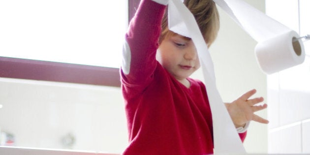 toddler boy playing with toilet paper in bathroom.