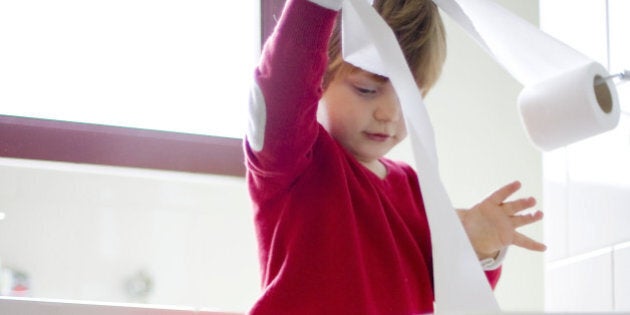 toddler boy playing with toilet paper in bathroom.