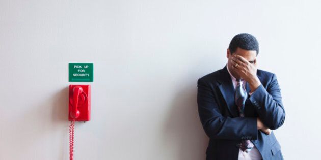 African American businessman leaning against wall covering his face