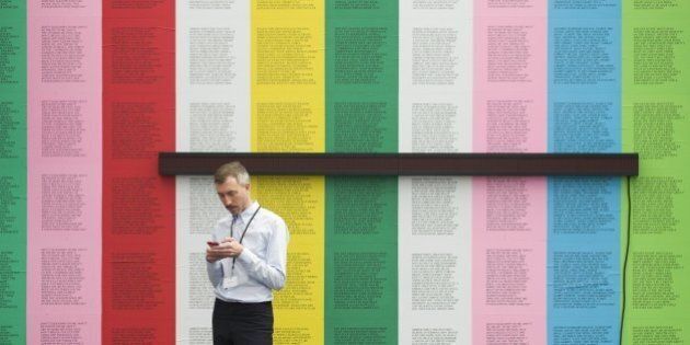 An exhibitor uses his phone standing in front of 'Survival' by US artist Jenny Holzwer at the Frieze Masters Art Fair in London on October 14, 2015. AFP PHOTO / JUSTIN TALLISRESTRICTED TO EDITORIAL USE, MANDATORY MENTION OF THE ARTIST UPON PUBLICATION, TO ILLUSTRATE THE EVENT AS SPECIFIED IN THE CAPTION (Photo credit should read JUSTIN TALLIS/AFP/Getty Images)