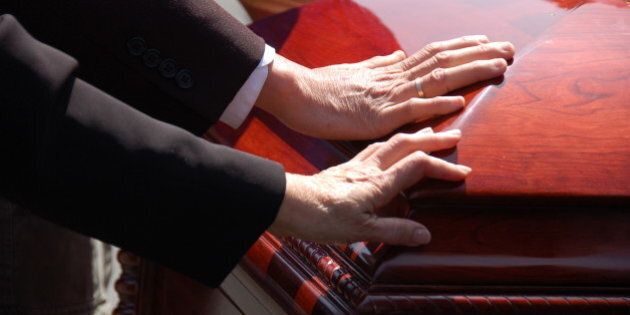 2 hands touching a closed wooden casket. Farewell to a loved one.