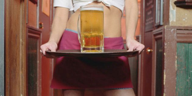 Young waitress holding glass of beer on tray, mid section