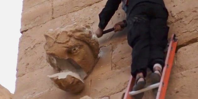 In this image made from a militant video posted on YouTube on Friday, April 3, 2015, which has been verified and is consistent with other AP reporting, a piece falls off from a curved face on the wall of an ancient building as a militant hammers it in Hatra, a large fortified city recognized as a UNESCO World Heritage site, 110 kilometers (68 miles) southwest of Mosul, Iraq. (AP Photo/Militant video)