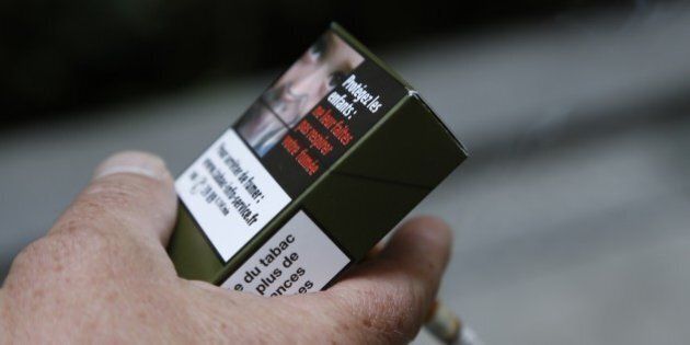 A man smokes a cigarette on September 25, 2014 in Paris, holding a sample of a 'plain cigarette packaging' cigarette box proposed by the 'Alliance contre le tabac' (alliance against tobacco) association. France on September 25 said it would introduce plain cigarette packaging and ban electronic cigarettes in certain public places, in a bid to reduce high smoking rates among the under-16s. Following a successful similar campaign in Australia, Health Minister Marisol Touraine said cigarette packets would be 'the same shape, same size, same colour, same typeset' to make smoking less attractive to young smokers. AFP PHOTO THOMAS SAMSON (Photo credit should read THOMAS SAMSON/AFP/Getty Images)