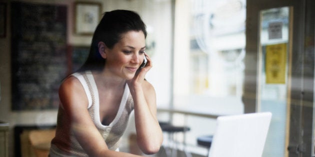 Young woman using mobile phone and laptop in coffee shop, smiling