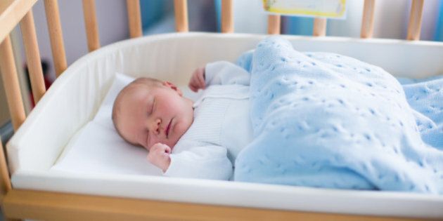 Newborn baby in hospital room. New born child in wooden co-sleeper crib. Infant sleeping in bedside bassinet. Safe co-sleeping in a bed side cot. Little boy taking a nap under knitted blanket.