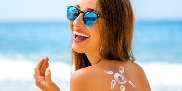 Young woman with sun shape on the shoulder holding sun cream bottle on the beach