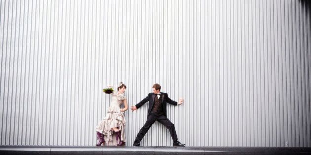 Playful bride and groom standing near wall