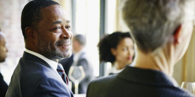 Smiling businessman sitting at table in restaurant listening during business lunch meeting