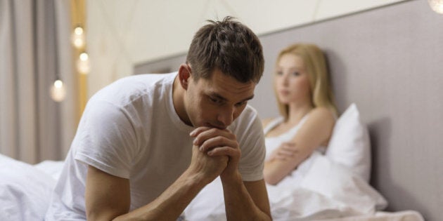 hotel, travel, relationships, and sexual problems concept - upset man sitting on the bed with woman on the back