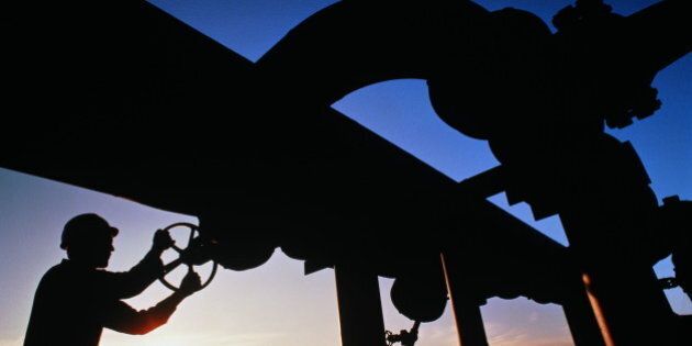 Worker turning valve on geothermal pipeline, silhouetted against dusk