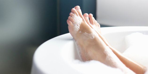 Feet resting on edge of tub as woman lays in a foam bath in a luxury hotel
