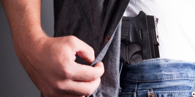 A man reveals a concealed pistol at his side.