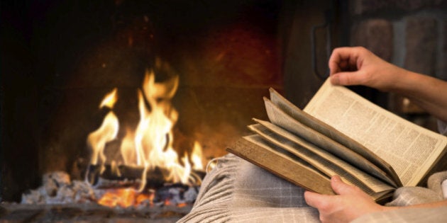 hands of woman reading book by fireplace