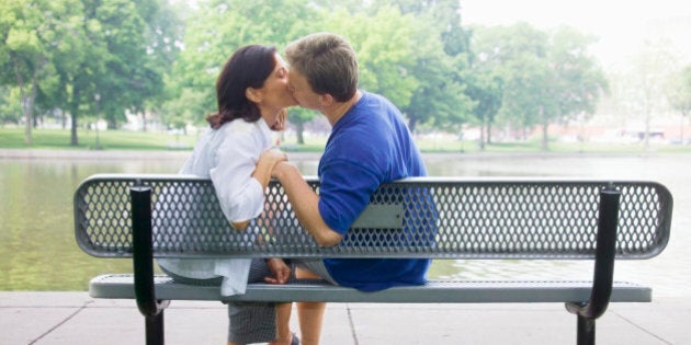 Parents kissing on bench in park