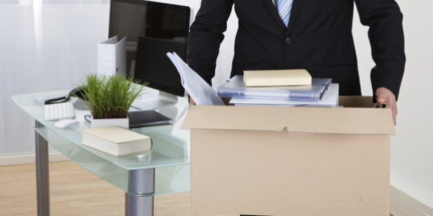 Businessman moving offices packing up all his personal belongings and files into a brown cardboard box