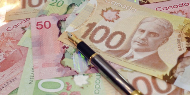 A fountain pen on a pile of Canadian $100 (hundred,) $50 (fifty,) and $20 (twenty) bills.