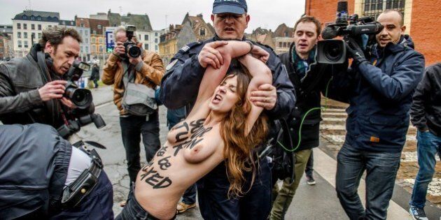 A Femen activist is detained by police after jumping in front of the car carrying former IMF chief Dominique Strauss-Kahn (not seen) upon his arrival for his trial in Lille, northern France, on February 10, 2015. Three topless women from the protest group Femen jumped on the car of Dominique Strauss-Kahn as the former IMF chief arrived to testify at his trial for 'aggravated pimping.' With slogans scrawled on their half-naked bodies and hurling insults at the car, the three protesters were quickly rounded up by police as the car entered an underground parking area. AFP PHOTO / PHILIPPE HUGUEN (Photo credit should read PHILIPPE HUGUEN/AFP/Getty Images)
