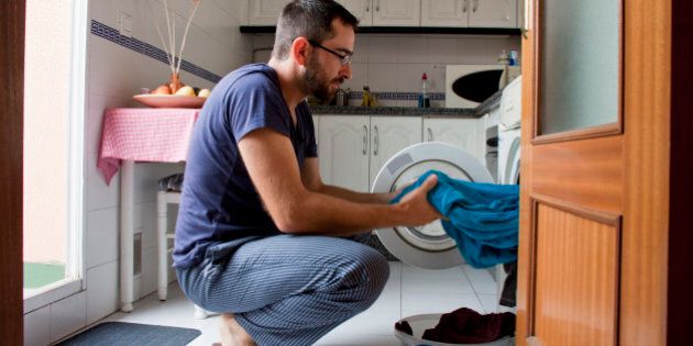 Close-up of man wearing blue pijama pulling towel from washing machine in kitchen.