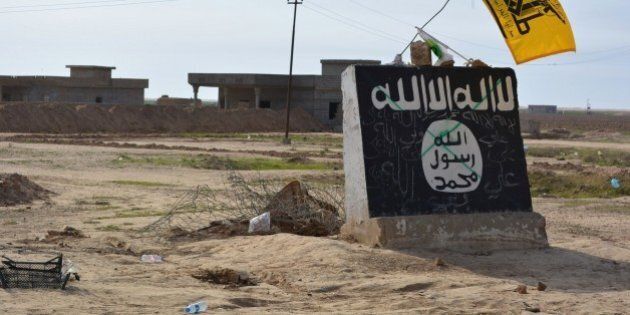 A flag of the Shiite Hezbollah militant group flutters over a mural depicting the emblem of the Islamic State (IS) group in Al-Alam village, northeast of the multi-ethnic Iraqi city of Tikrit, on March 9, 2015, during a military operation by Iraqi government forces and tribal fighters to regain control of the Tikrit region from jihadists. After being forced out of the province of Diyala earlier this year, the IS jihadists are now fighting off a huge assault on the city of Tikrit as government and allied forces continue to work their way north towards the main IS stronghold of Mosul. AFP PHOTO / YOUNIS AL-BAYATI (Photo credit should read YOUNIS AL-BAYATI/AFP/Getty Images)