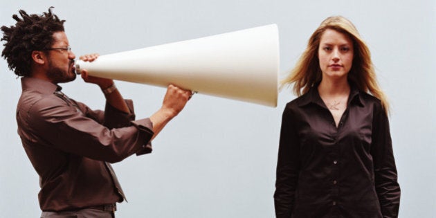 Man yelling into megaphone pointed at young woman's ear