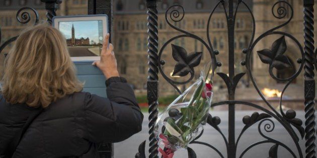 A lady takes a photo through the Queen's Gate at Canada's House of Parliament in Ottawa on Thursday evening October 23, 2014, one day after multiple shootings in the capital city and Parliament buildings left a soldier dead and others wounded. A gunman whose name was on a terror watch list killed a soldier and attempted to storm Canada's parliament October 22 before the assembly's sergeant-at-arms shot him dead. The attack -- the second this week targeting Canadian military personnel -- came as Canadian jets were to join the US-led bombing campaign against Islamist militants in Iraq.. AFP PHOTO/PETER MCCABE (Photo credit should read Peter McCabe/AFP/Getty Images)