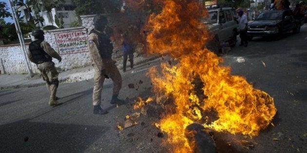 Haitian police remove a barricade of burning tires placed by anti-government protesters during a march against the government of Haitian President Michel Martelly in Port-au-Prince, on January 10, 2015. Protesters marched through the streets calling for the resignation of the Haitian leader. On January 12, Haiti marks the fifth anniversary of a catastrophic earthquake that killed 300,000 people, but also a dangerous new stage in its political crisis. The sitting parliament in the impoverished Caribbean nation will come to the end of its mandate and no date has been set for new elections, leaving a perilous political vacuum. Protesters accuse Martelly of tacitly allowing the parliament to expire in order to rule by decree, while he accuses the opposition of blocking an electoral law that would allow a vote. AFP PHOTO/Hector RETAMAL (Photo credit should read HECTOR RETAMAL/AFP/Getty Images)