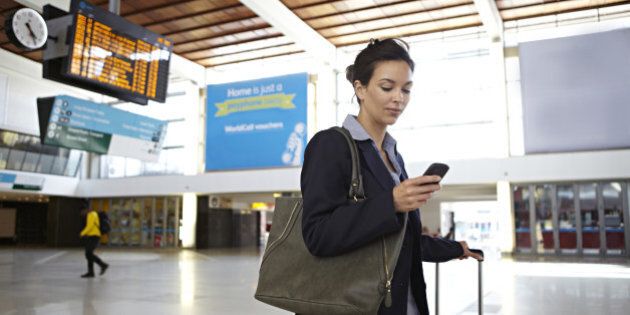 Businesswoman looking at smart phone in train station foyer