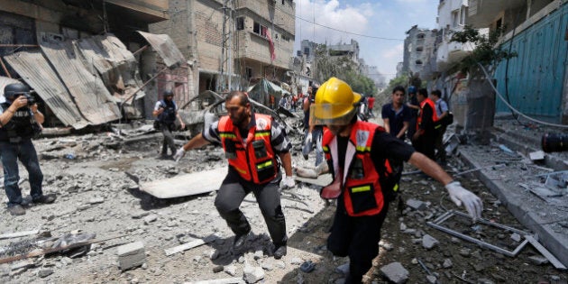 Palestinian medics carry a casualty as they run past a burning building in Gaza City's Shijaiyah neighborhood, northern Gaza Strip, Sunday, July 20, 2014. Dozens of people were killed in Shijaiyah and more bodies were believed buried under the rubble of homes, health officials said. (AP Photo/Lefteris Pitarakis)