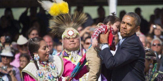 US President Barack Obama (R) picks up a child as he poses with Native American performers during the Cannon Ball Flag Day Celebration in Cannon Ball, North Dakota, June 13, 2014. AFP PHOTO / Jim WATSON (Photo credit should read JIM WATSON/AFP/Getty Images)