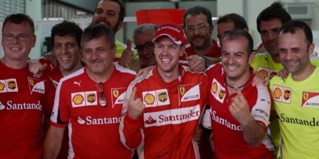 Ferrari's German driver Sebastian Vettel (C) poses for pictures along with his team members after winning the Formula One Malaysian Grand Prix in Sepang on March 29, 2015. AFP PHOTO / MOHD RASFAN (Photo credit should read MOHD RASFAN/AFP/Getty Images)