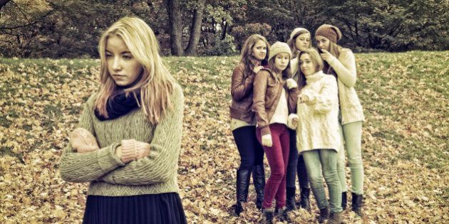 This is a major issue in school, rejection and intimidation between students. Here is a group of five friends gossiping behind the back of a visibly sad rejected girl. Desaturated effect.