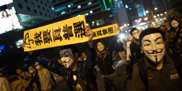 HONG KONG - NOVEMBER 05: Pro-democracy protesters wear Guy Fawkes mask as they hold banners and shout slogans on a street near Hong Kong Government Complex in Admiralty district on November 5, 2014 in Hong Kong. Pro-democracy protesters staged a rally on Guy Fawkes day. (Photo by Anthony Kwan/Getty Images)
