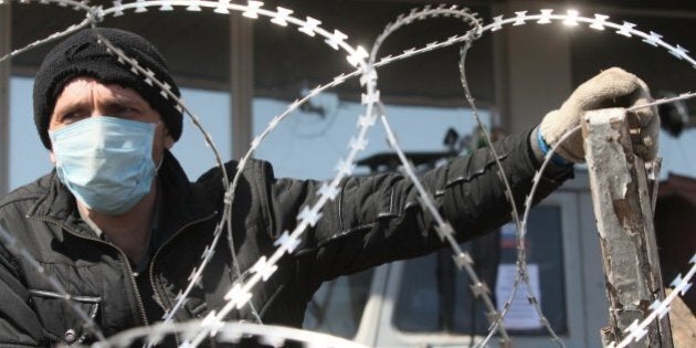 A pro-Russian militant wearing a surgical mask guards a barbed wire covered barricade in front of the Donetsk regional administration building on April 8, 2014. Ukraine mounted a counteroffensive on April 8 by vowing to treat the separatists as 'terrorists' and making 70 arrests in a nighttime security sweep, while hundreds of militants remained holed inside the Donetsk administration building a day after proclaiming the creation of an independent 'people's republic' and demanding that an independence referendum be held before May 11. AFP PHOTO / ALEXANDER KHUDOTEPLY (Photo credit should read Alexander KHUDOTEPLY/AFP/Getty Images)