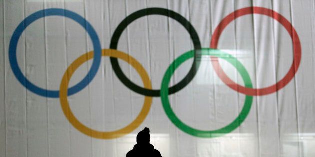 A man is silhouetted against the Olympic Rings as he walks to the venue for the women's normal hill ski jumping final at the 2014 Winter Olympics, Tuesday, Feb. 11, 2014, in Krasnaya Polyana, Russia. (AP Photo/Charlie Riedel)
