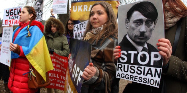 Demonstrators wear the Ukrainian flag and hold posters reading 'Hands off Ukraine' and featuring Russian President Vladimir Putin as German nazi dictator Adolf Hitler during a protest against Russia's intervention in Ukraine in front of the Russian embassy in Vilnius, on March 3, 2014.AFP PHOTO / PETRAS MALUKAS (Photo credit should read PETRAS MALUKAS/AFP/Getty Images)