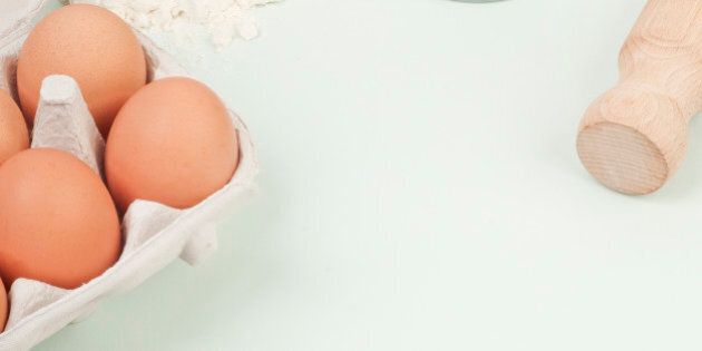 Eggs in eggbox, broken eggshell, white flour spilling from bag, and part of rolling pin
