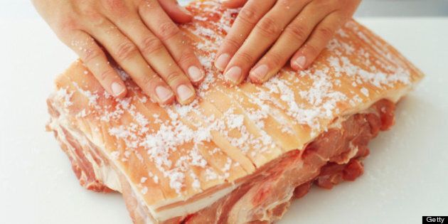 Sea salt being rubbed into scored rind of pork joint, high angle view