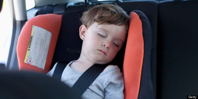 A young boy sleeping in a car seat in the back seat of a car