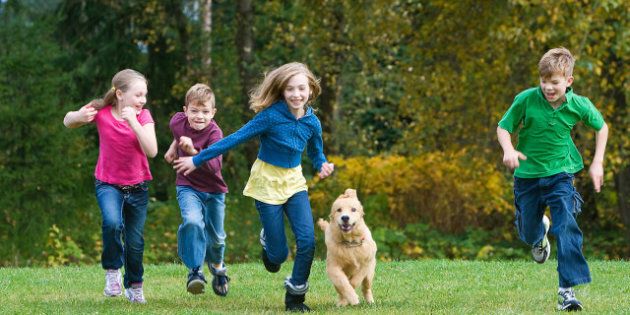 A group of 4 kids racing in a park with a dog.