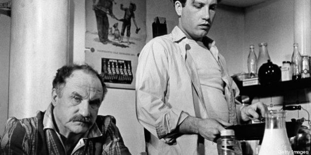 Jack Warden sitting at a dining table while Richard Dreyfuss is standing beside him holding a pan in a scene from the film 'The Apprenticeship of Duddy Kravitz', 1974. (Photo by Paramount Pictures/Getty Images)
