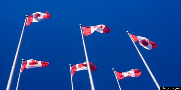 Canadian flags on tall poles against a blue sky