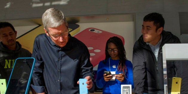 Tim Cook, chief executive officer of Apple Inc., second left, adjusts an Apple Inc. iPhone 5c displayed during the launch of the device at the company's new Stanford Shopping Center store in Palo Alto, California, U.S., on Friday, Sept. 20, 2013. Apple Inc. attracted long lines of shoppers at its retail stores today for the global debut of its latest iPhones, in the company's biggest move this year to stoke new growth. Photographer: David Paul Morris/Bloomberg via Getty Images