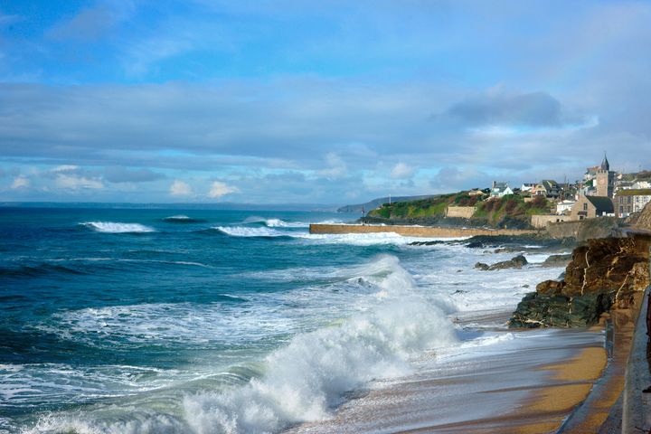 Waves breaking on the beach at Porthleven on a winters day looking towards the clock tower, Cornwall, England, UK